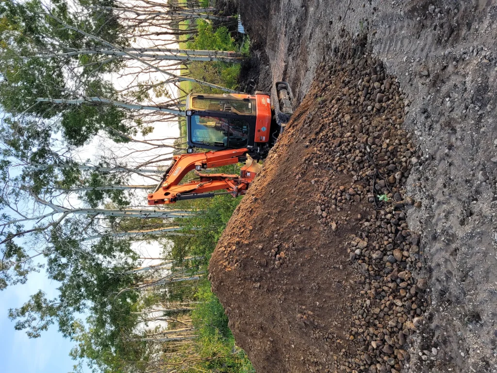 Excavator carving a trench alongside a residential foundation for drainage repair