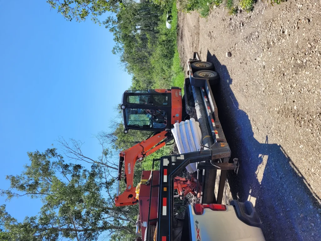 Excavator carving a trench alongside a residential foundation for drainage repair